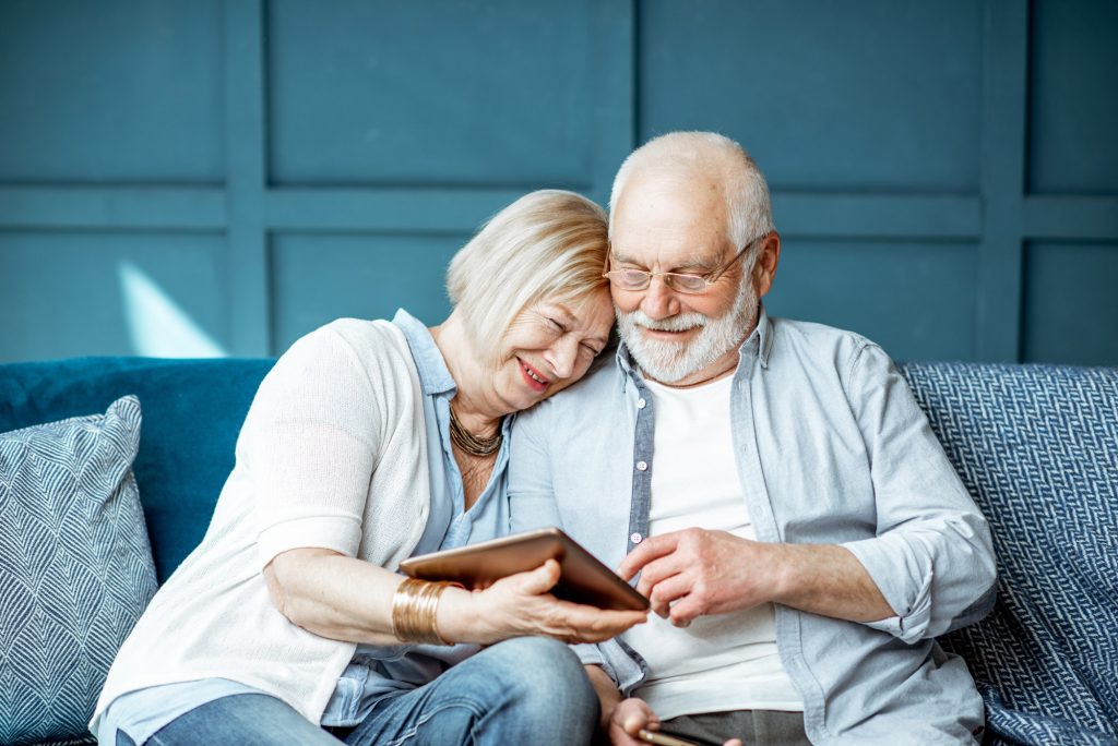 Lovely senior couple dressed casually using digital tablet while sitting together on the comfortable couch at home