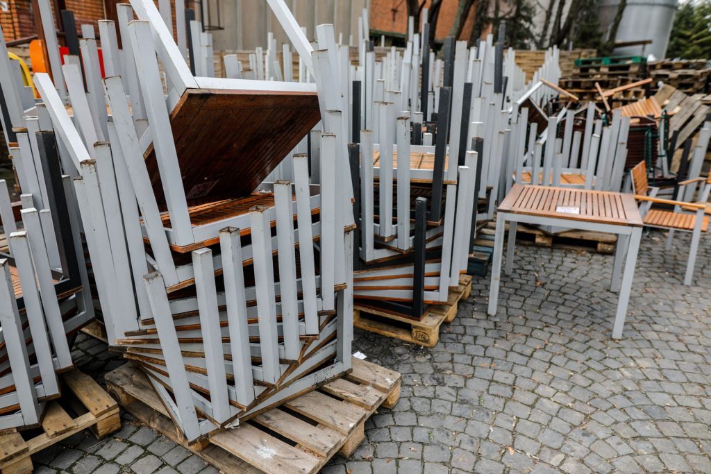Pile of old restaurant iron and wooden tables stacked outside the restaurant on a cloudy winter day.